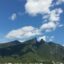 a mountain top covered in green trees touches the cloudy sky