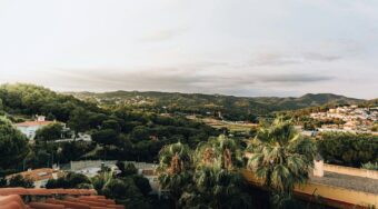View of Lloret de Mar, showing hills with trees and houses, and a body of water in the distance.