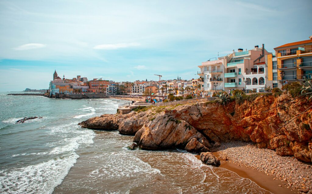 View of Sitges on the coast, with homes lining the waterfront and and blue skies above.