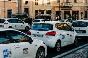 Taxi Rome - Welcome Pickups A queue of white Rome taxis on either side of a road in the city.