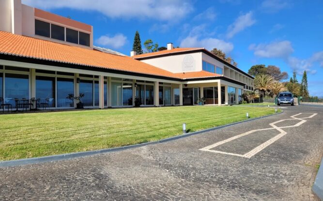 The entrance to the Albatroz Beach & Yacht Club at Madeira Airport painted a pale yellow with a terracotta roof and a green lawn and road in front.