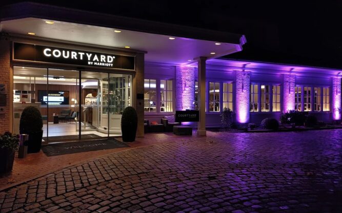 The Courtyard Hotel at Hamburg Airport lit up at night with purple and white lighting.