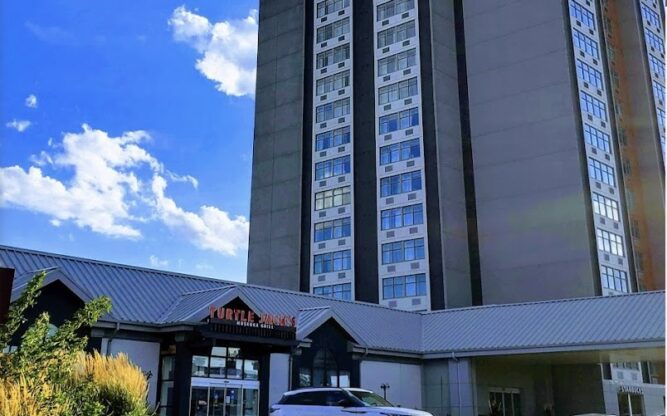 A tall building with a green lawn in front and a car parked by the entrance