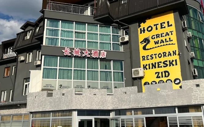 The glass-walled entrance to the Great Wall Hotel at Sarajevo Airport with a yellow sign featuring a snake.