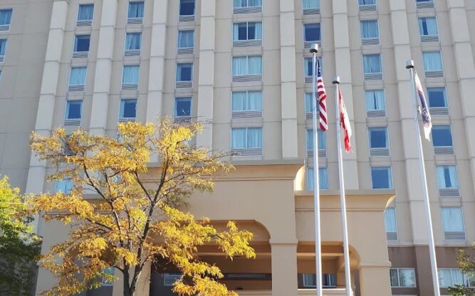The front view of the Hampton Inn & Suites Hotel near Toronto Airport with autumn trees and two flagpoles in front