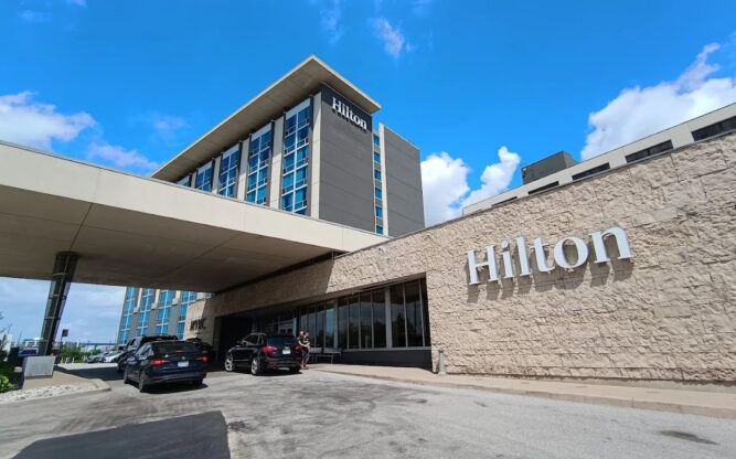 A driveway with two black vans leading up to the entrance of the tall Hilton Toronto Airport Hotel.