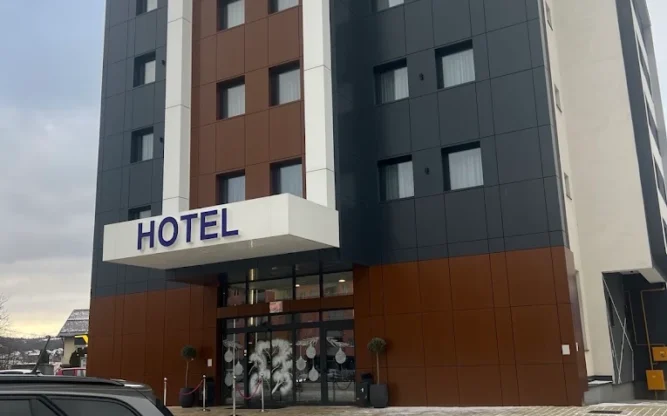 The brown and blue Hotel Brčko Gas Istočno building with a car parked in front and snow on the ground.