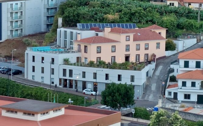 A view of the yellow and gray Hotel Solar Bom Jesus at Madeira Airport set on a hill surrounded by other roads and other hotels.