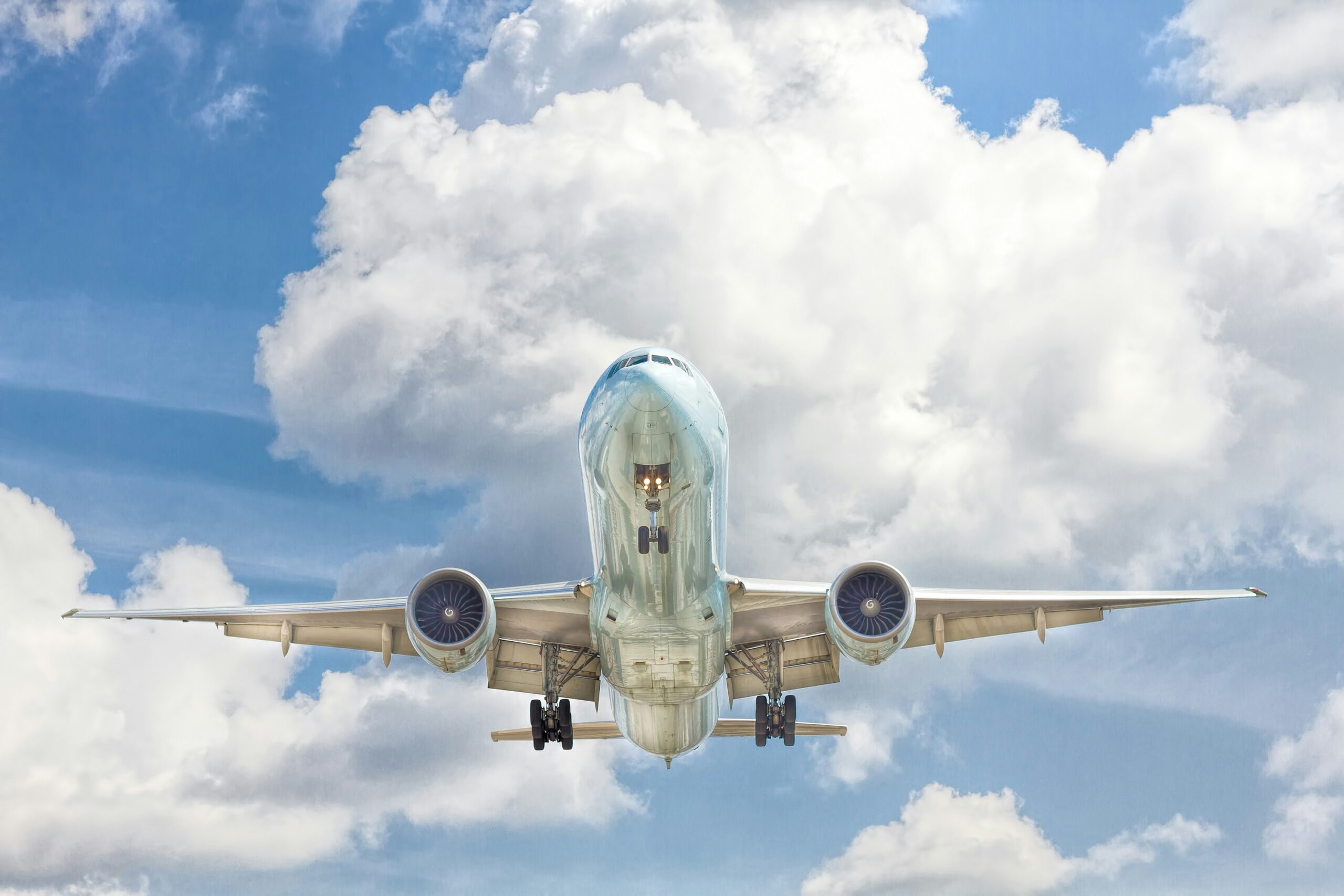 a silver passenger plane flies overhead under a bright white cloud