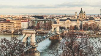 Scenic view of central Budapest featuring the iconic Chain Bridge over the Danube River, with historic buildings and St. Stephen's Basilica in the background—part of the route from Budapest Airport to the main train station.