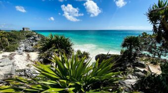 Panoramic view of Tulum’s rocky coastline and turquoise Caribbean Sea, featuring ancient Mayan ruins and lush greenery—highlighting the natural beauty awaiting travelers going to Tulum from Cancun Airport.