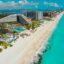 Aerial view of a beachfront resort and turquoise coastline in Cancun City, with luxury hotels, pools, palm trees, and white sand stretching along the shoreline.