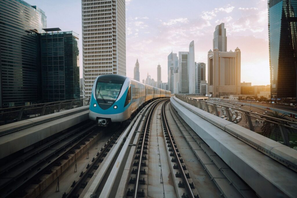 Dubai Airport Metro train traveling along elevated tracks at sunset, with the city’s modern skyscrapers in the background. A scenic and efficient transport option connecting Dubai International Airport to the city center.