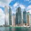 A daytime view of Dubai Marina with modern skyscrapers and luxury yachts docked along the waterfront, a popular destination easily reached via DWC Airport transfer.