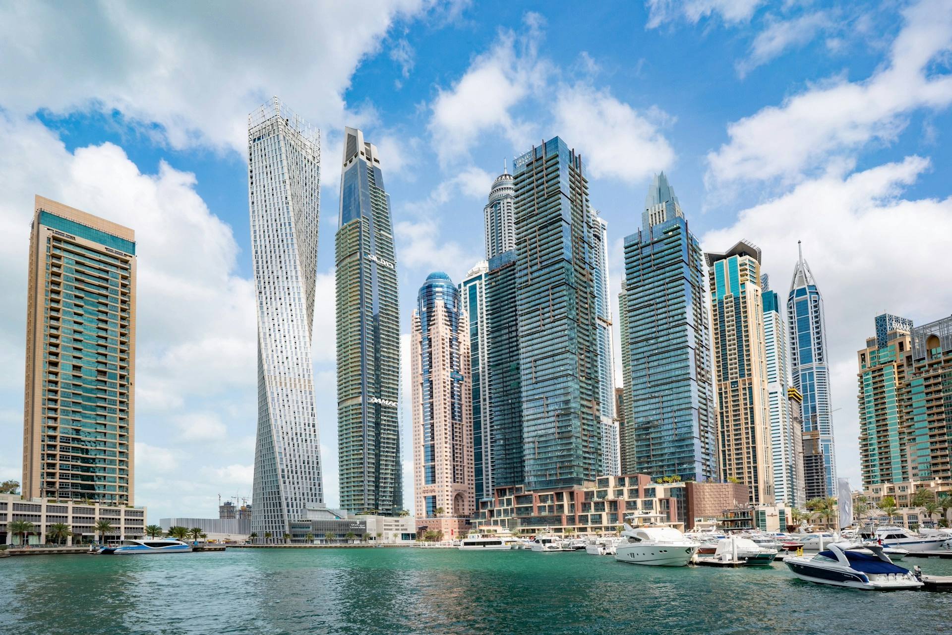 A daytime view of Dubai Marina with modern skyscrapers and luxury yachts docked along the waterfront, a popular destination easily reached via DWC Airport transfer.