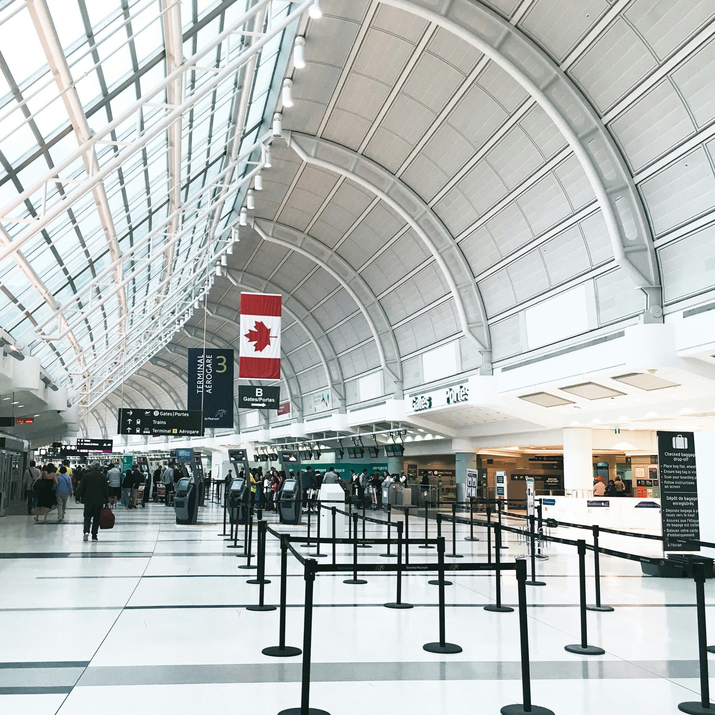 view inside Toronto Airport entrance with ropes set up to form lines in front of check in desks under a half-dome sky lit roof