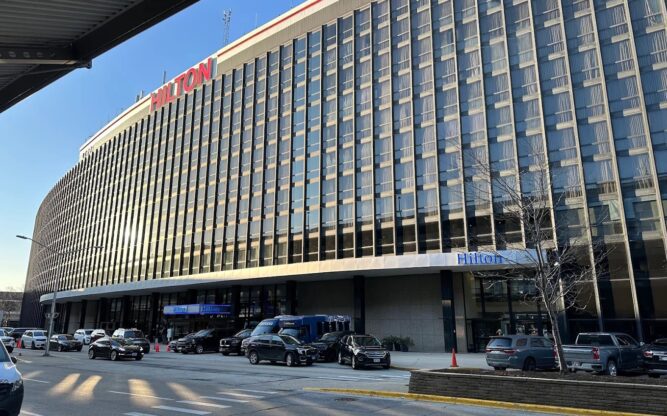 The tall and slightly curved Hilton Hotel at Chicago Airport with a red sign on top of the building.