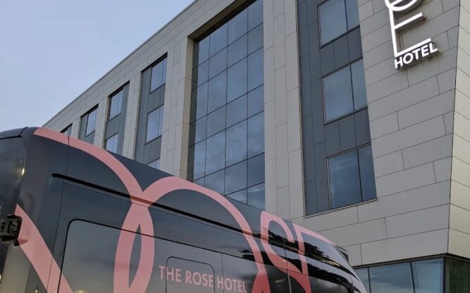 A black van with the "Rose Hotel" logo parked in front of the gray Rose Hotel building.