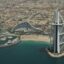 Aerial view of Dubai’s iconic Burj Al Arab and Jumeirah Beach Hotel with turquoise waters, yacht marina, and city skyline in the background—highlighting the scenic drive when going from Al Maktoum Airport to Dubai.