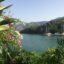 Lush greenery and vibrant flowers frame a serene coastal view in Fethiye, Turkey, with sailing boats anchored in calm turquoise waters beneath a clear sky; capturing the region’s natural beauty and tranquil Mediterranean atmosphere.