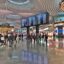 Busy interior of Istanbul New Airport with travelers walking past luxury shops and a large digital departures board under a modern, curved ceiling.