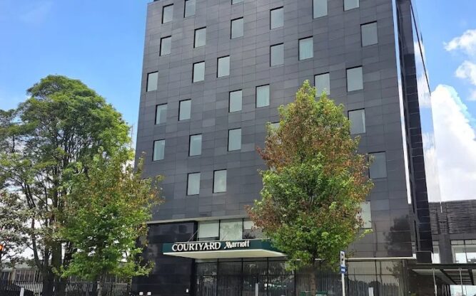 A tall gray building with lots of windows with a grassy park in front.