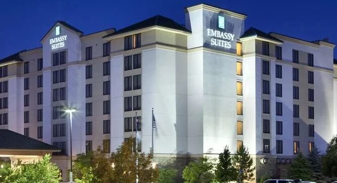 A view of the Embassy Suites at Denver Airport lit up at night with bushes surrounding the property