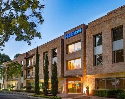 The Habitel Hotel near Bogota Airport lit up at dusk with a large tree hanging over the building