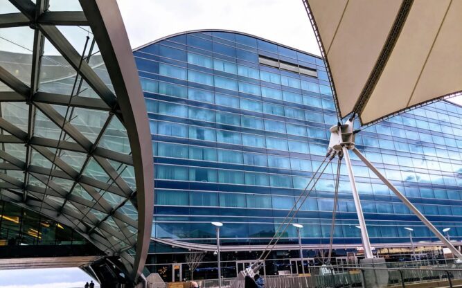 A huge glass building obstructed by part of a sail and a curved steel structure.