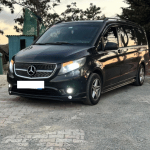 A black Mercedes van with headlights on, parked on a quiet roadside at sunset—commonly used as an airport taxi in Istanbul for convenient city and airport rides.