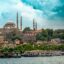 Scenic daytime view of Istanbul’s historic Süleymaniye Mosque rising above a lively mix of waterfront buildings, trees, and docked boats along the Golden Horn — a striking first impression for travelers enjoying an airport transfer in Istanbul.
