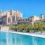 La Seu Cathedral in Palma de Mallorca stands tall beside a palm-lined waterfront on a clear, sunny day—an iconic view for travelers arriving via a Mallorca Airport to Palma transfer.