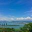 A view of an ocean inlet surrounded by trees and a blue sky with scattered clouds