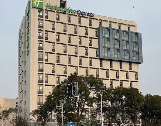 A tall beige hotel building with lots of windows, and trees lining the perimeter.