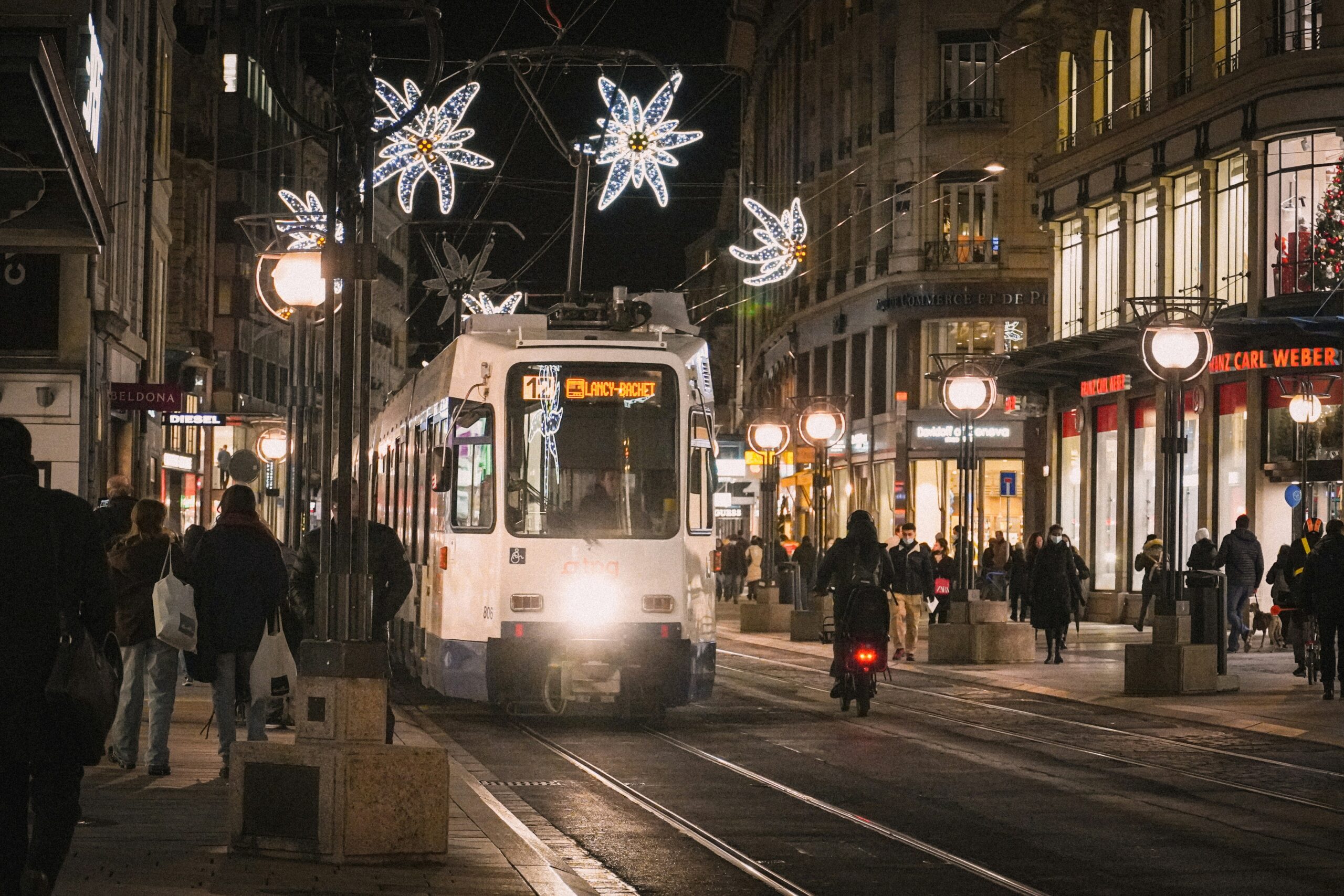 A tram driving down the street in Geneva at night, surrounded by Christmas lights.