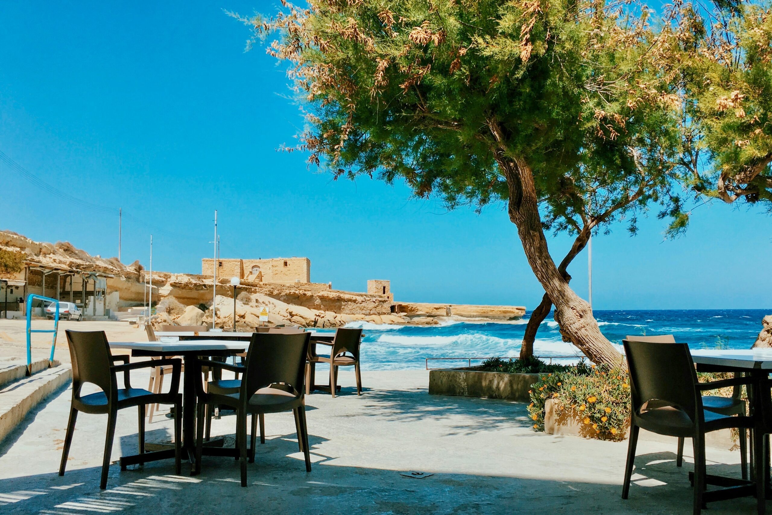 dining tables and chairs set up in the shade alongside one of Malta's beautiful beaches
