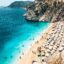 A golden sandy beach covered in beach chairs surrounded by crystal blue waters and large rocky cliffs.