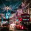 A busy street lit up with Christmas lights shaped like angels with a big red bus and lots of cars.