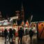 People walking past a lit up stall at the Vienna Christmas Market at night.
