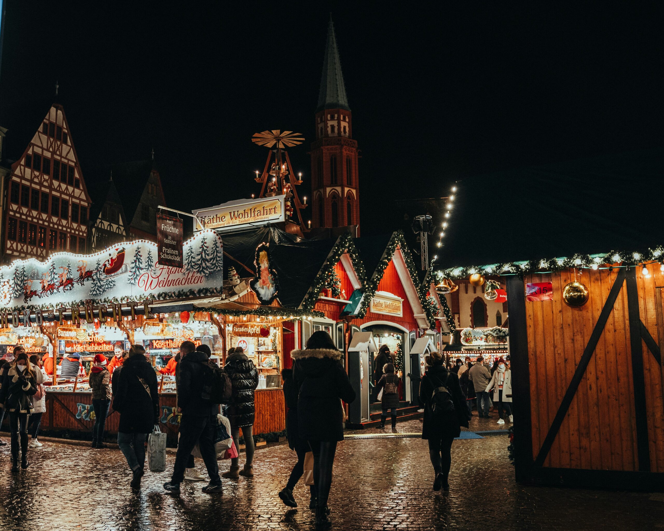 People walking past a lit up stall at the Vienna Christmas Market at night.