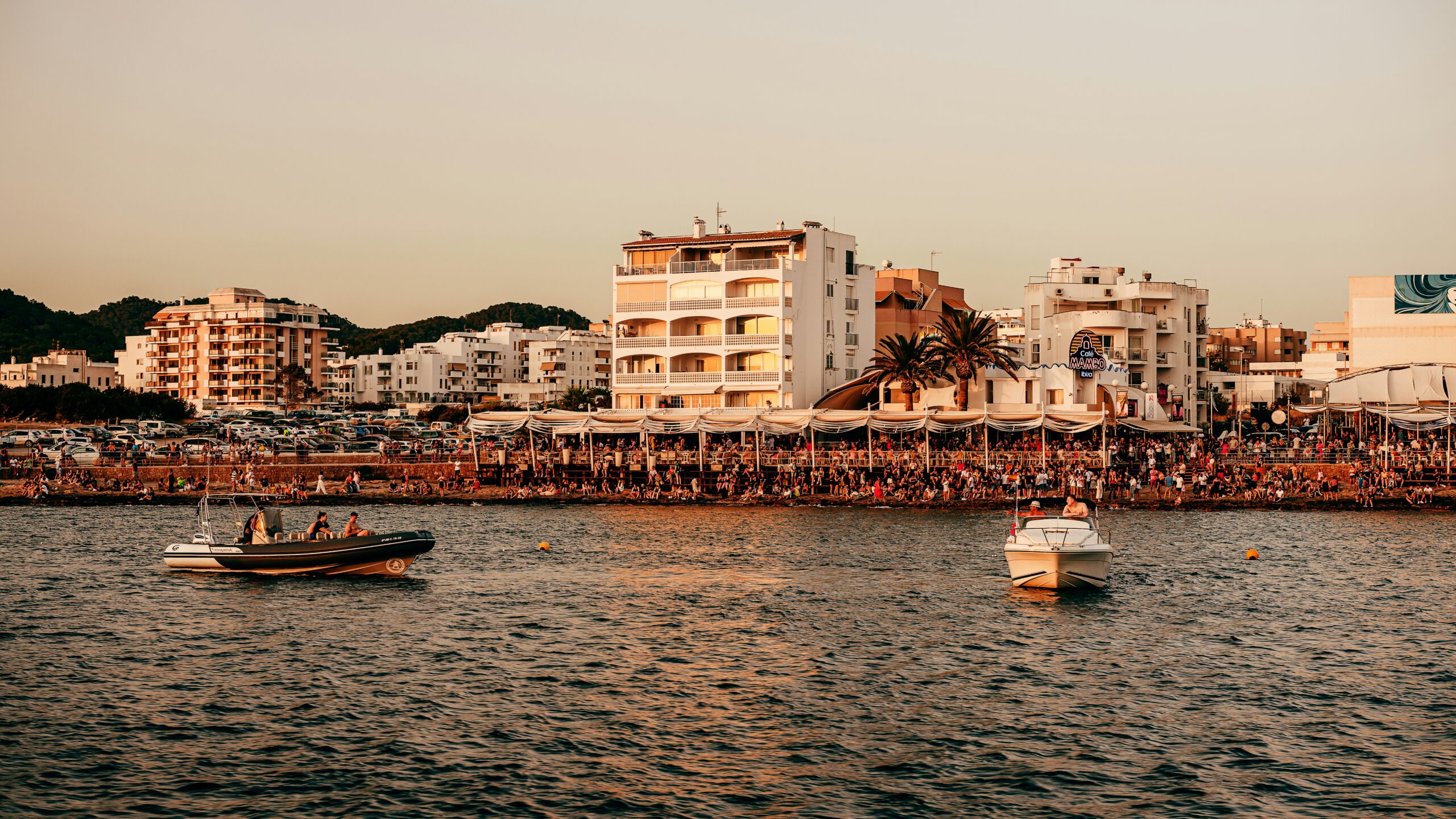 A view of the coastline in Ibiza with lots of people on the beach and boats in the water.