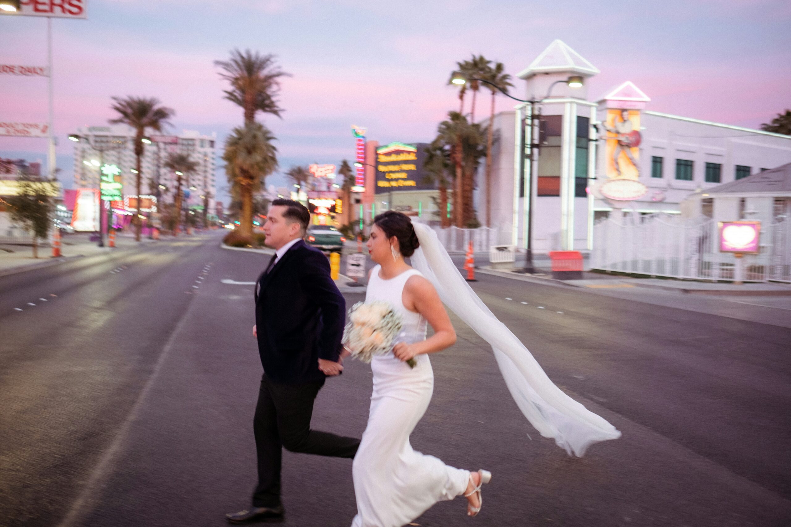 A married couple in a dress and suit crossing an empty street in downtown Las Vegas