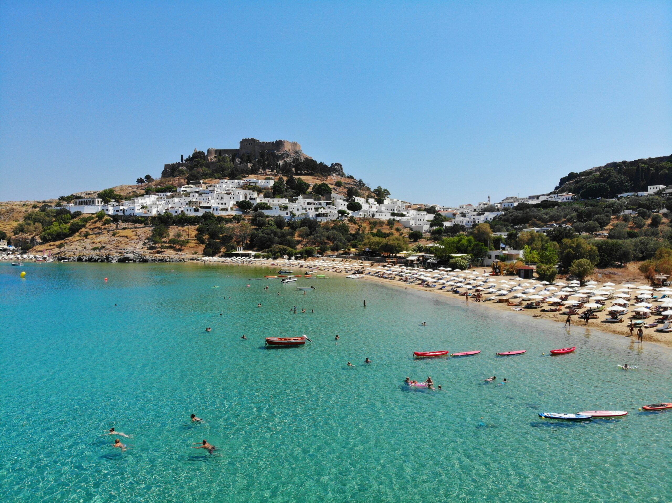 A beach with crystal clear waters surrounded by a cliff with white houses and a castle