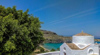 A white house and a tree framing a bay set against a rugged mountainside.