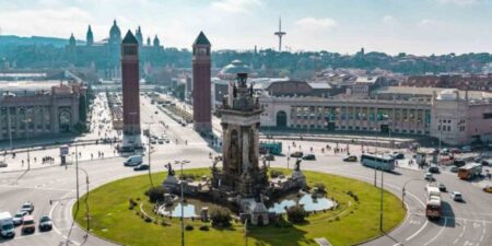 View of a grassy roundabout in central Barcelona, with cars on the road, and two towers bordering one of the exits.