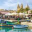Traditional colorful Luzzu boats in the harbor of Marsaxlokk, Malta, with the parish church in the background; a top destination for travelers booking a Malta airport taxi.