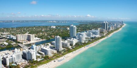 Aerial view of Miami Beach's coastline and luxury high-rise hotels along the turquoise Atlantic Ocean, a top destination for travelers booking a Miami airport taxi.