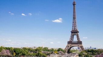 The Eiffel Tower and Champ de Mars in Paris, France, under a clear blue sky; a premier destination for travelers booking a Paris Airport taxi to their hotel.