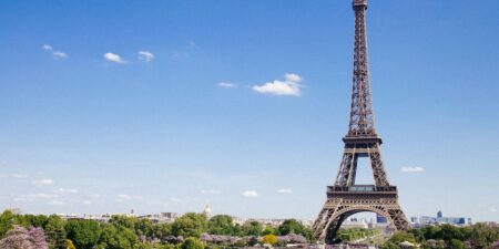The Eiffel Tower and Champ de Mars in Paris, France, under a clear blue sky; a premier destination for travelers booking a Paris Airport taxi to their hotel.