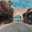 The iconic entrance of Mandraki Harbor in Rhodes, Greece, with the deer statues and medieval fortress; a top location for travelers booking a Rhodes airport taxi.